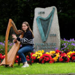Girl sitting with harp in landscaped garden with large sculpture behind her